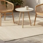 A markiseteppe outdoor mat styled on a patio with rattan chairs and potted plants in natural daylight