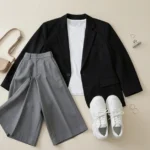 A flat-lay acubi aesthetic outfit with wide-leg grey trousers, a white baby tee, boxy black blazer, and chunky sneakers