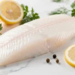 Fresh Alaskan Seiti Alaska pollock fillet with lemon and herbs on white marble surface