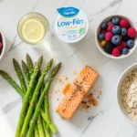 A flat lay of gout diet foods including tart cherries, water, low-fat yogurt, salmon, oats, and fresh vegetables on a white marble surface