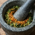 Stone mortar and pestle with picada paste made from toasted almonds, garlic, and fresh parsley on a rustic wooden surface