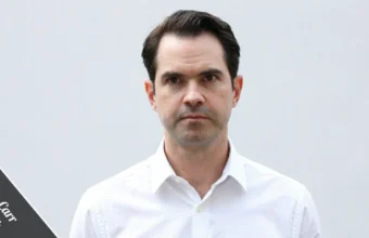 Jimmy Carr in a sharp charcoal suit leans against a black Rolls-Royce, with the London skyline behind him, representing his £25 million Jimmy Carr net worth and comedy career.